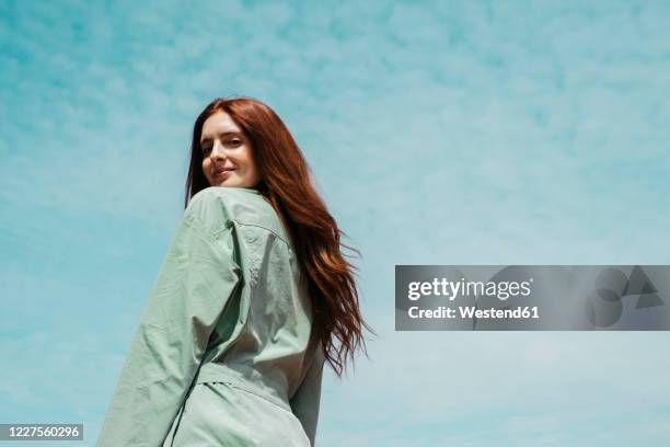 portrait of redheaded young woman against sky - beauty woman hair stock-fotos und bilder
