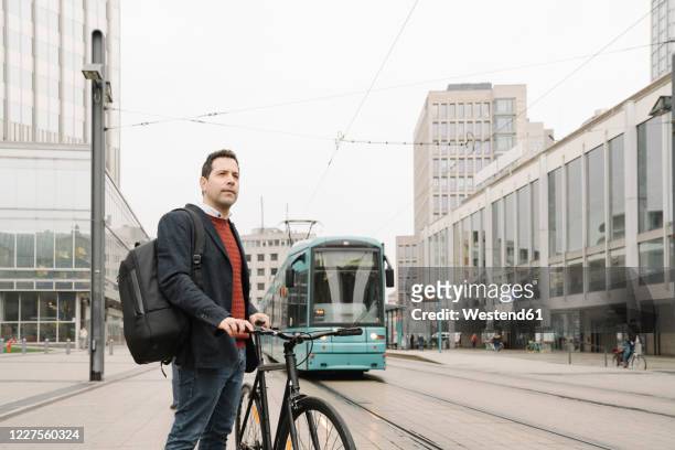 entrepreneur with bicycle standing against cable car in city, frankfurt, germany - hesse germany stock-fotos und bilder