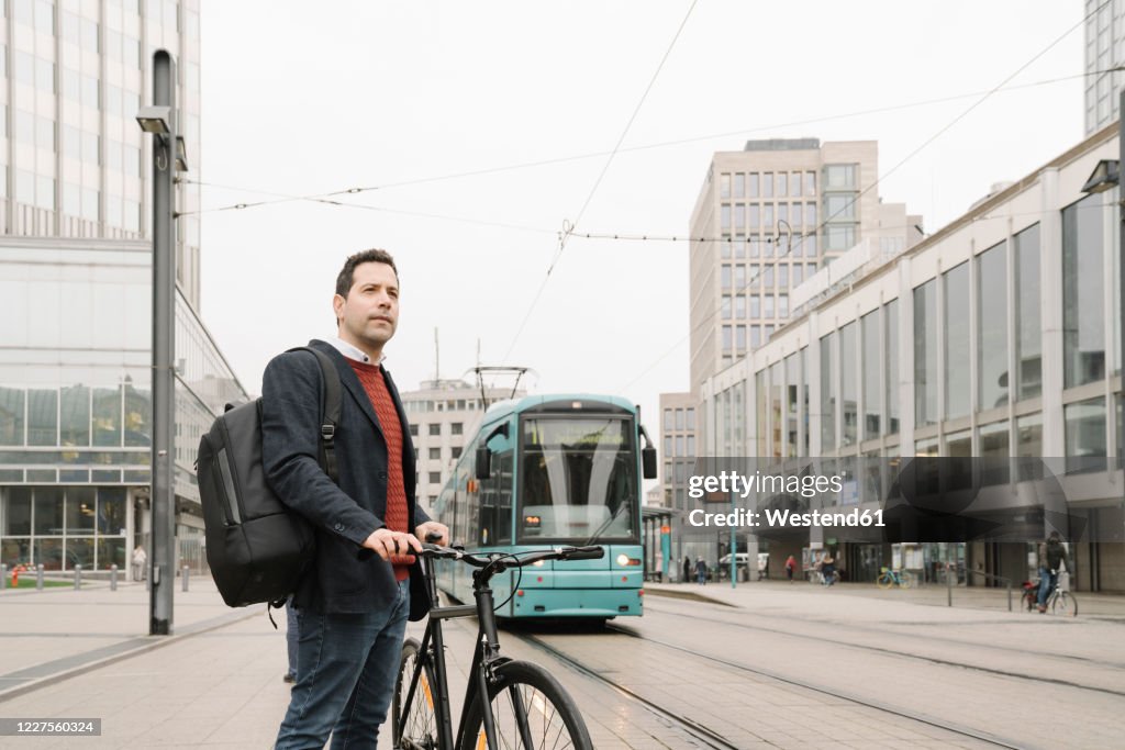 Entrepreneur with bicycle standing against cable car in city, Frankfurt, Germany