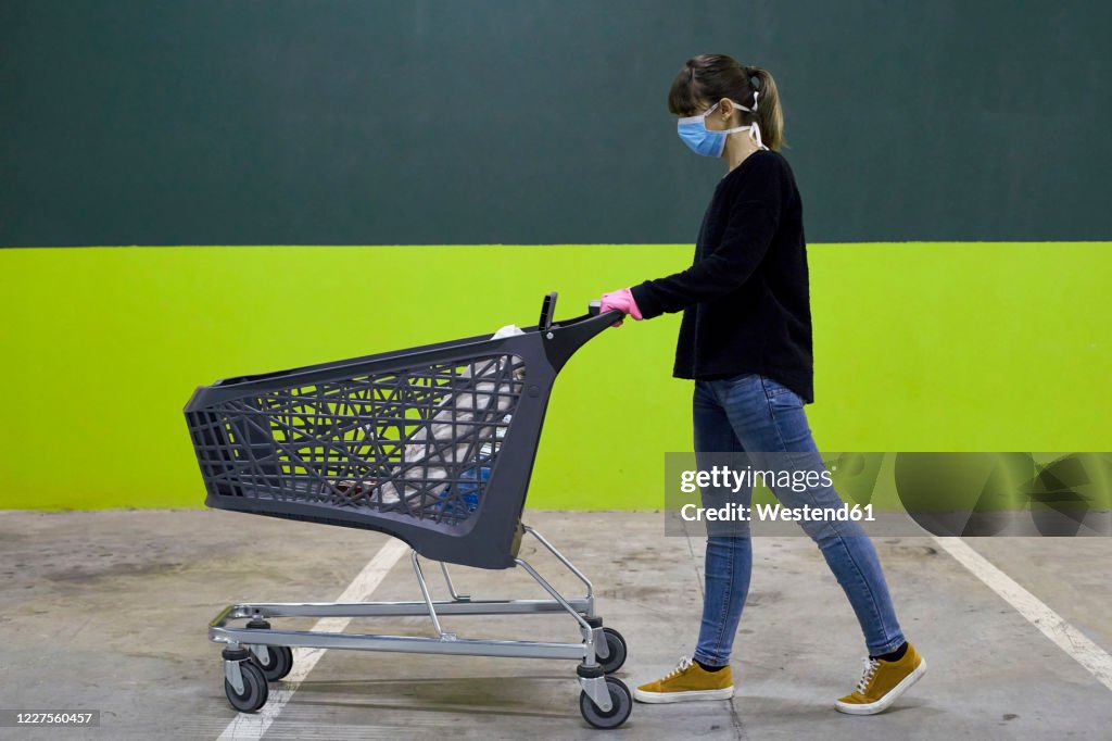 Woman wearing mask walking with shopping cart against wall