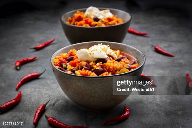 red chili peppers and two bowls of vegetarian chili with red lentils, kidney beans, tomatoes, carrots, celery and sour cream - celeriac stockfoto's en -beelden