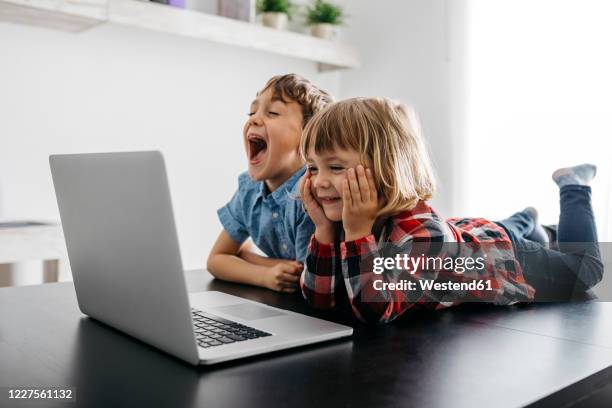 happy girl and boy lying on desk looking at laptop - brother toddler sister stockfoto's en -beelden