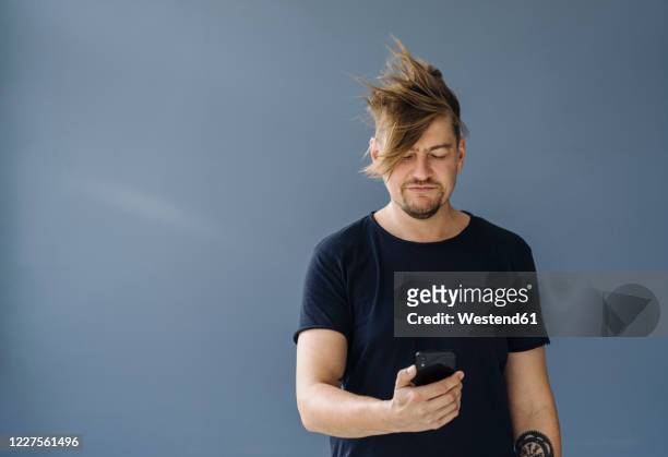 bearded man with tousled hair using smartphone - hair flying stock-fotos und bilder