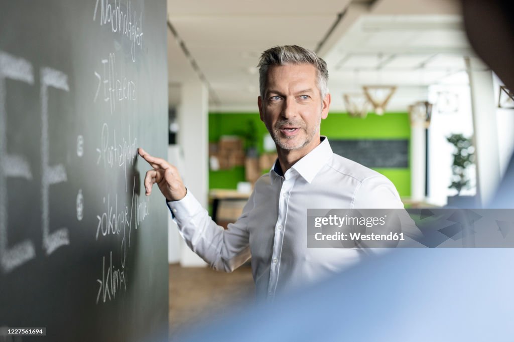 Mature businessman brainstorming at blackboard in office