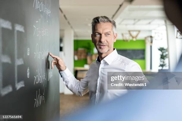 mature businessman brainstorming at blackboard in office - dialog und bildung stock-fotos und bilder