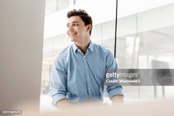 portrait of smiling young businessman at the window in office - junge männer stock-fotos und bilder