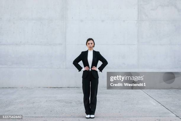 young woman wearing black suit standing in front of concrete wall - casacos pretos imagens e fotografias de stock