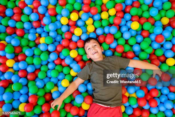 smiling boy lying in ball pit - ball pit stock pictures, royalty-free photos & images