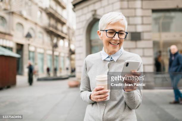 elderly woman in the city, using a smart phone - banking stock pictures, royalty-free photos & images