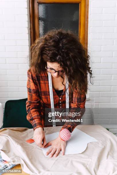 woman pinning sewing pattern on table at home - schnittmuster stock-fotos und bilder