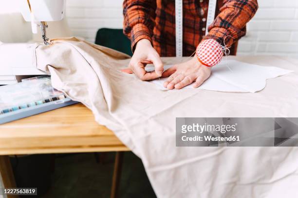 close-up of woman pinning sewing pattern on table at home - pinning stock pictures, royalty-free photos & images