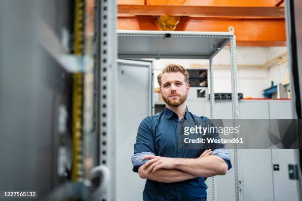 portrait of a confident young man in a factory - rolling up sleeve stock-fotos und bilder
