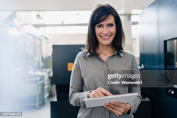 portrait of a smiling businesswoman using a tablet in a factory - grey blouse stock pictures, royalty-free photos & images