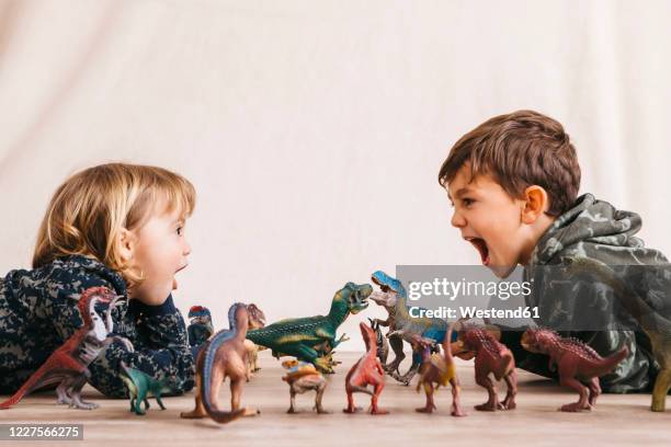 brother and his little sister playing with toy dinosaurs - hermano hermana fotografías e imágenes de stock