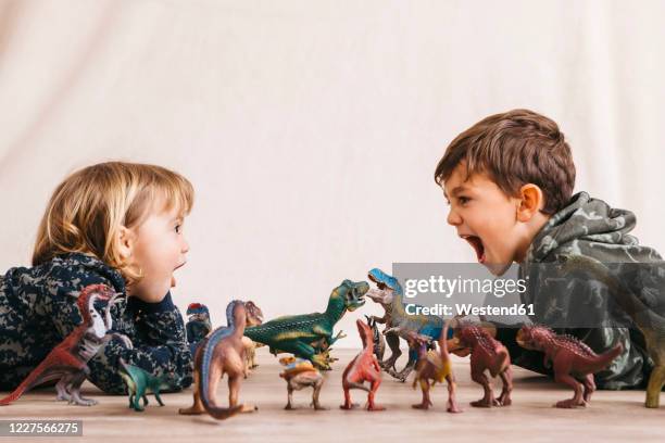 brother and his little sister playing with toy dinosaurs - brother sister stock pictures, royalty-free photos & images