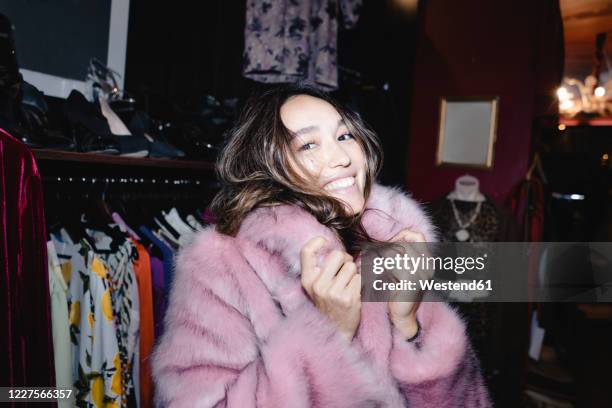 portrait of smiling woman wearing pink fur jacket at thrift store - fur jacket imagens e fotografias de stock