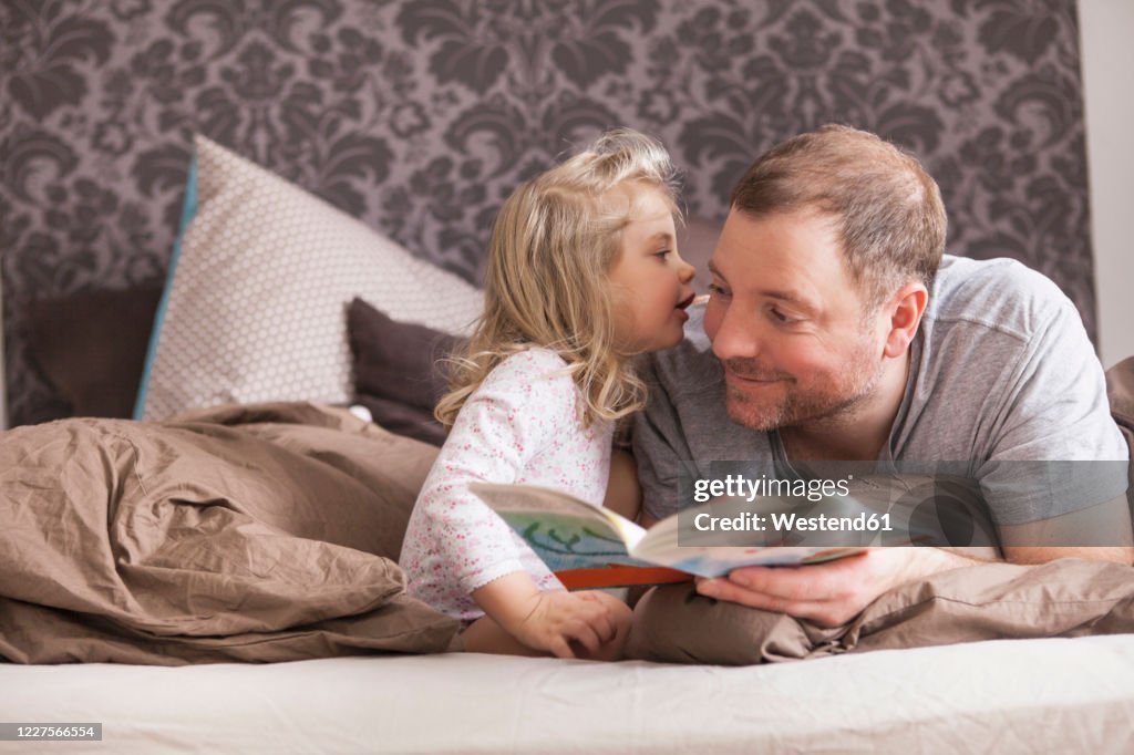 Father and daughter reading a book in bed, whispering in ear