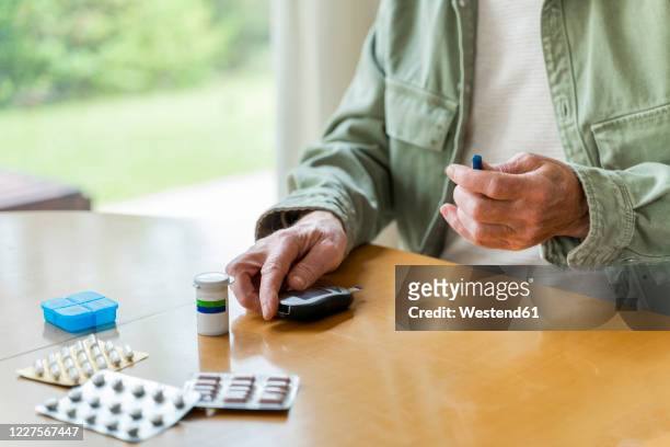 midsection of retired diabetic senior man examining himself while sitting at table - diabetes pills stock pictures, royalty-free photos & images