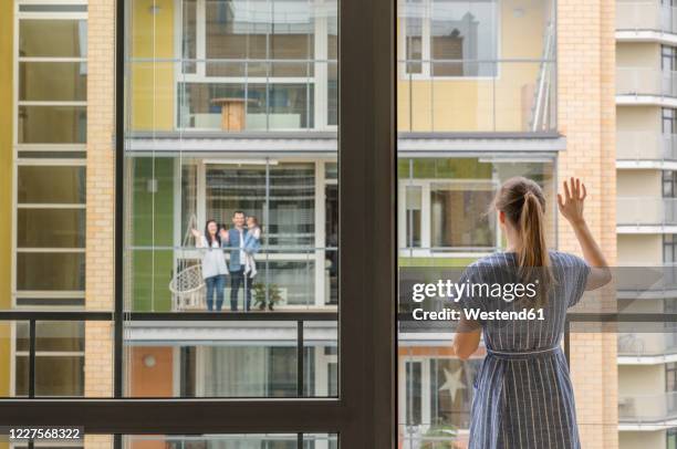 back view of woman standing on balcony waving to her neighbours - nachbar stock-fotos und bilder