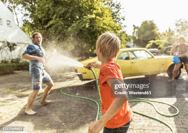 friends washing yellow vintage car in summer having fun - car splashing water on people stock pictures, royalty-free photos & images