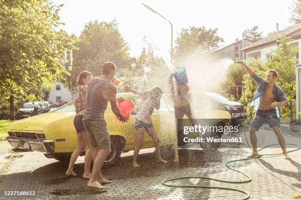 group of friends washing yellow vintage car in summer having fun - car wash ストックフォトと画像