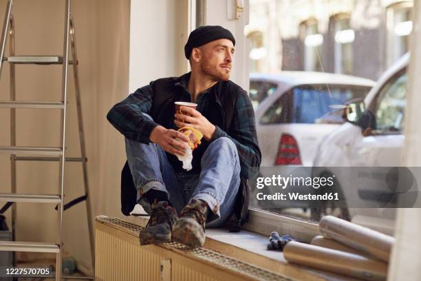 man refurbishing shop location, sitting on windowsill, drinking coffee - artisan food stock-fotos und bilder