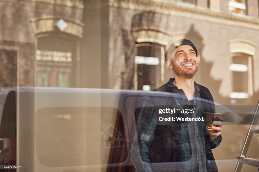 Man refurbishing shop location, drinking coffee, looking out of window