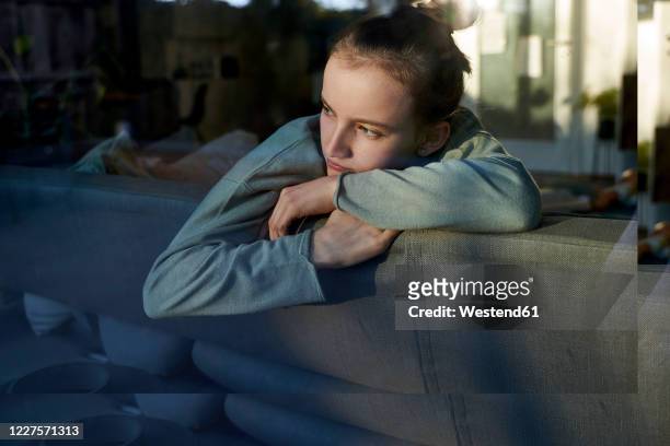 serious girl on couch at home looking out of window - sadgirl stock-fotos und bilder