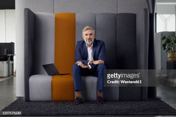 portrait of mature businessman sitting on couch in office - sitzen stock-fotos und bilder