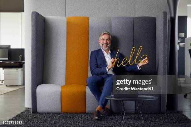 portrait of smiling mature businessman sitting on couch in office holding hello sign - welcome sign ストックフォトと画像