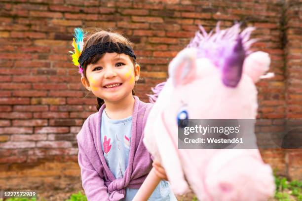 portrait of girl with braids and feather headdress riding a pink unicorn - toy animal stock pictures, royalty-free photos & images