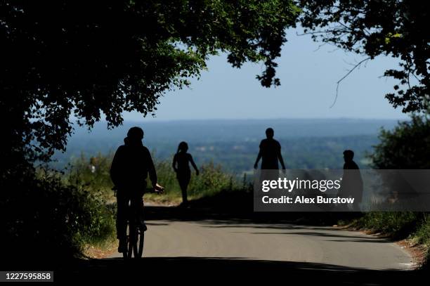 Silhouette of a cyclist and some walkers as they make their way along Zig Zag road on Box Hill on May 28, 2020 in Tadworth, England. The British...