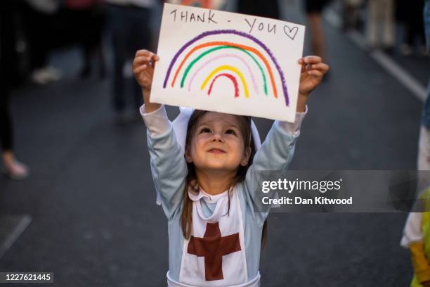 Maria Sole dressed in a small nurses outfit holds up a rainbow drawing with the words 'Thank You' on it as NHS staff and members of the public take...