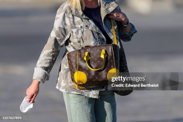 Passerby wears a gray military camouflage print jacket, a brown and yellow monogram leather Vuitton bag, on May 28, 2020 in Paris, France.