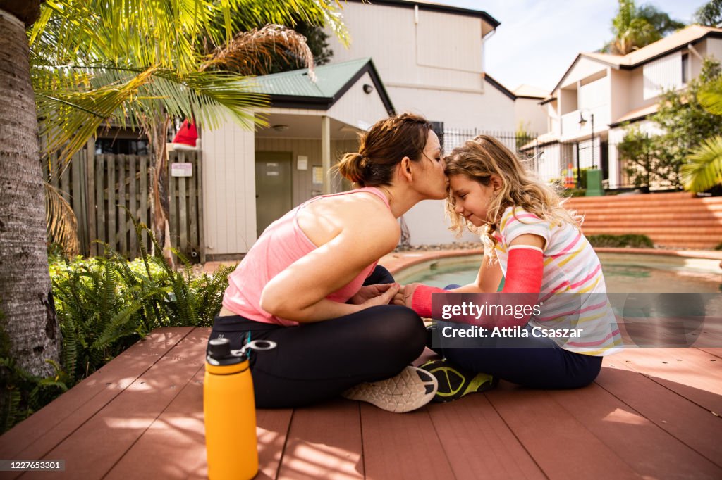 Mother giving kiss to injured daughter in cast at pool