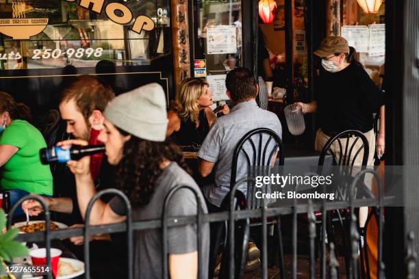 Server wearing a protective mask and gloves speaks with customers at the outside seating area of a restaurant in downtown Asheville, North Carolina,...