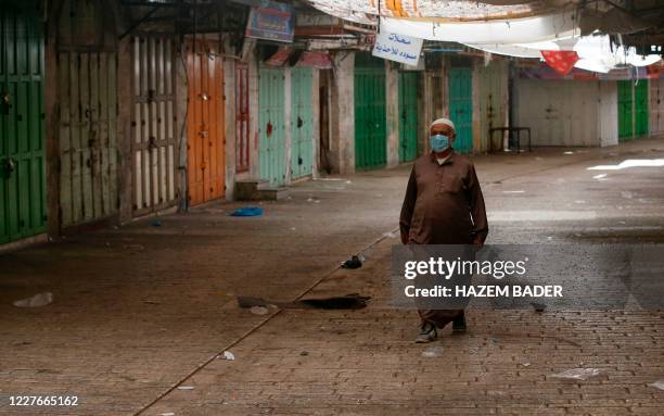 Palestinian man walks in front of closed shops in the centre of the West Bank city of Hebron on July 17 after a surge in coronavirus cases. - For...