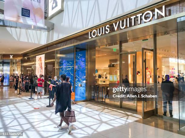 Shoppers wear masks while waiting in line to shop at Louis Vuitton at South Coast Plaza Monday, which will be closed down Tuesday for a second time...
