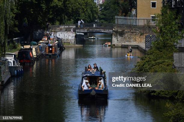 People enjoy the sunshine as they travel on a narrow boat along Regent's Canal, near Victoria Park in east London, on July 18, 2020.