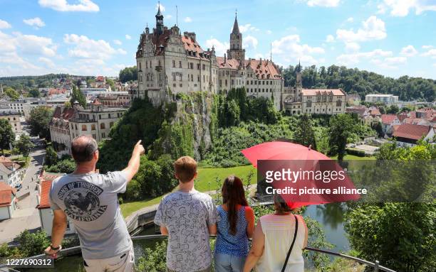 July 2020, Baden-Wuerttemberg, Sigmaringen: A family with a parasol in their hands is standing on a viewing platform opposite Sigmaringen Castle....