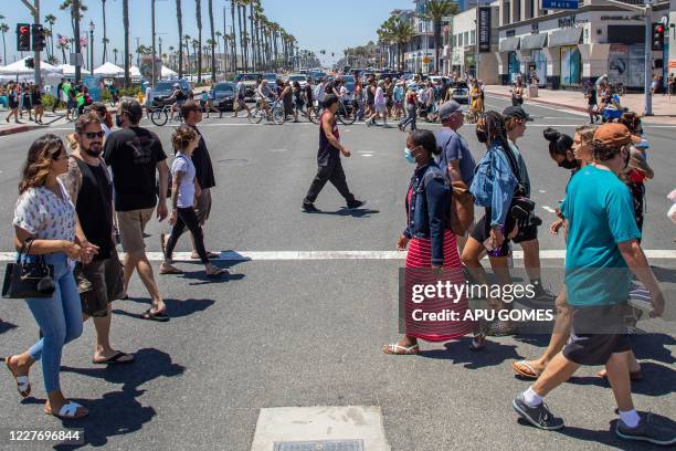 People cross the street in Huntington Beach, California, on July 19, 2020 amid the coronavirus pandemic. - The United States today, June 19 recorded...