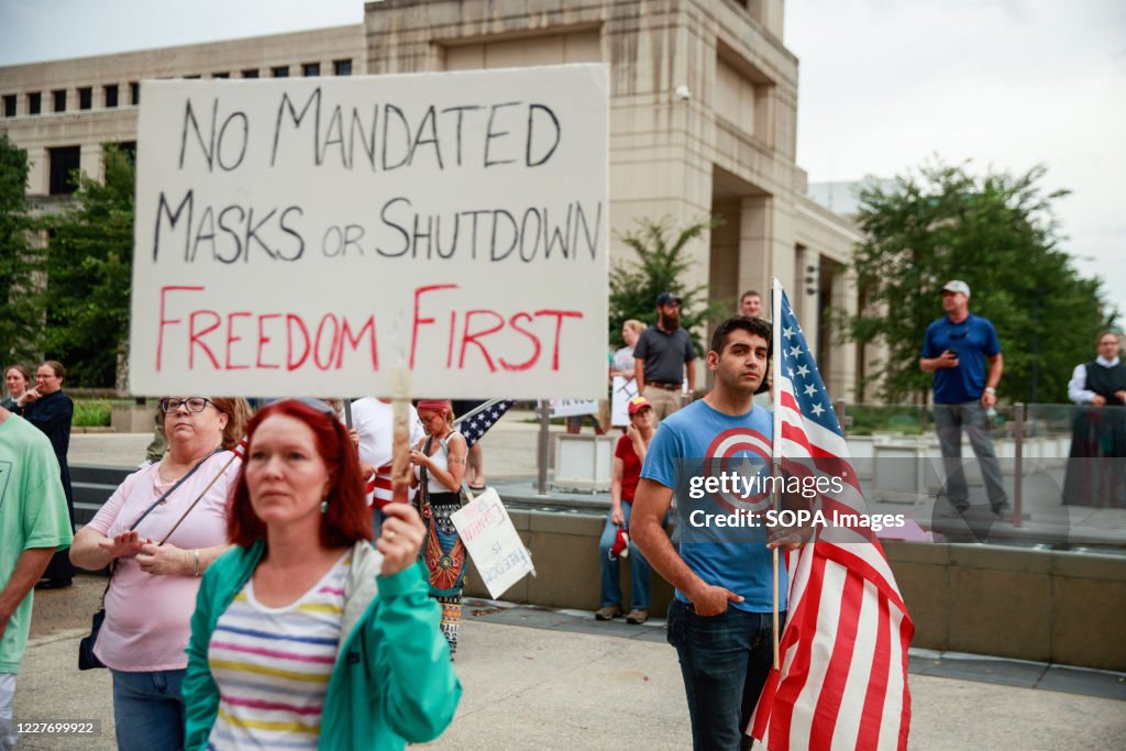 A protester holds a placard saying No Mandated Masks or...