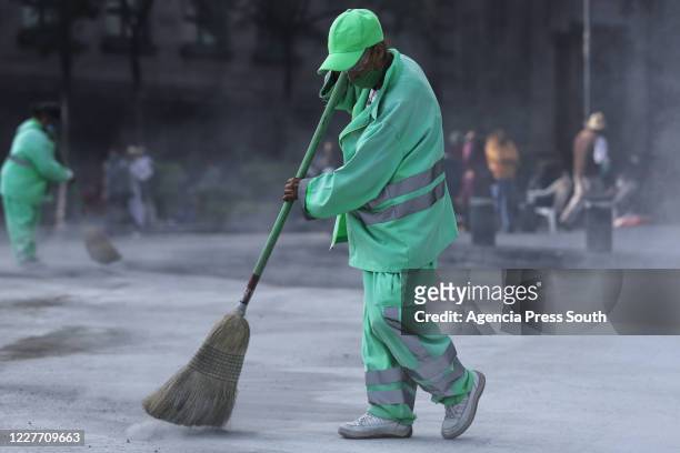 Cleaning company worker sweeps the floor wearing protective mask and glasses during maintenance work to replace the asphalt around the Plaza de la...