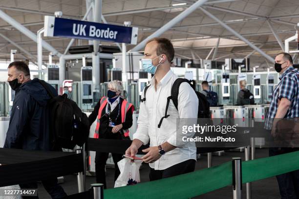 Passengers in protective face masks queue at the passport control after arriving at London Stansted Airport as the United Kingdom is trying to take...
