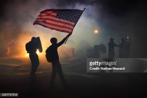 Protester flies an American flag while walking through tear gas fired by federal officers during a protest in front of the Mark O. Hatfield U.S....