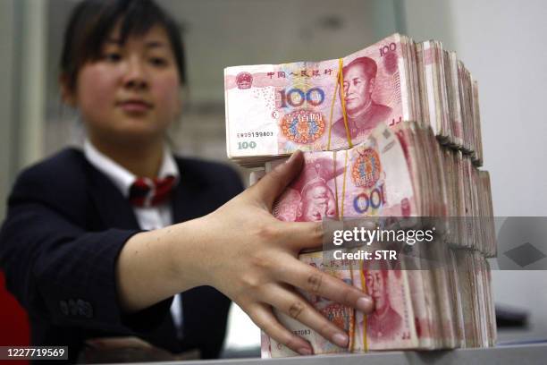 Chinese bank worker arranges stacks of 100-yuan notes at a bank in Suining, southwest China's Sichuan province on March 20, 2010. By pushing China...
