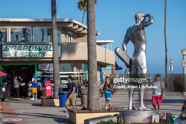 People walk, ride and skateboard on the sidewalk past businesses and the the Ben Carlson memorial statue near the pier on a summer day Monday, July...