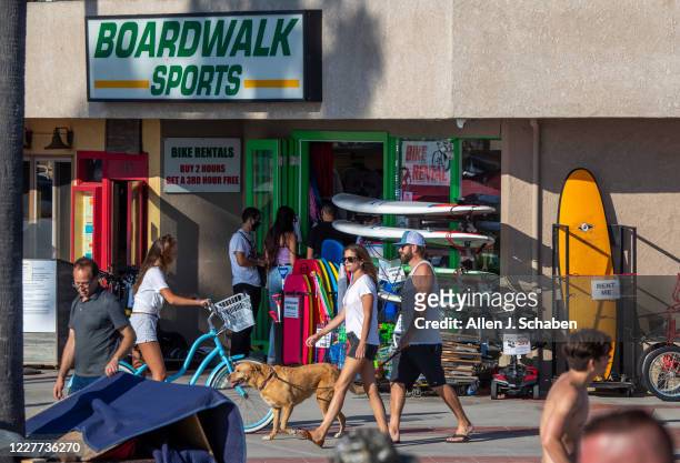 People walk, ride and skateboard on the sidewalk past businesses on a summer day Monday, July 20, 2020 in Newport Beach, CA.