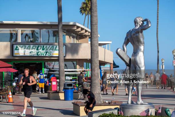 People jog, ride and skateboard on the sidewalk past businesses and the the Ben Carlson memorial statue near the pier on a summer day Monday, July...