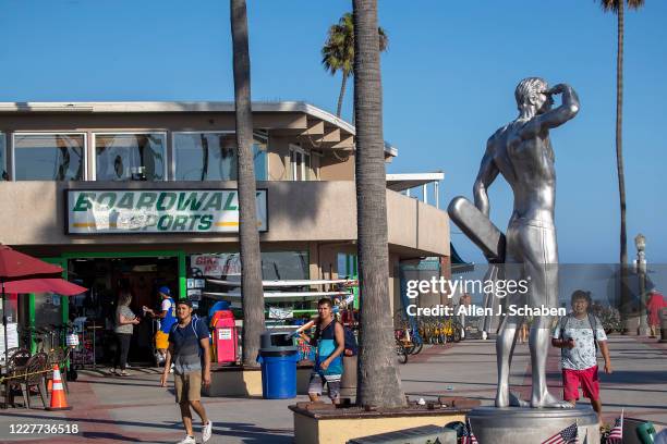 People walk, ride and skateboard on the sidewalk past businesses and the the Ben Carlson memorial statue near the pier on a summer day Monday, July...